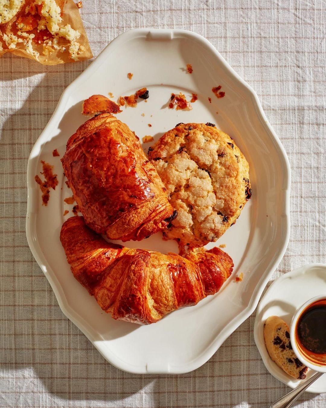 Overhead shot on a table featuring two croissants, a scone, and a cup of coffee, arranged on a white plate with a linen tablecloth.