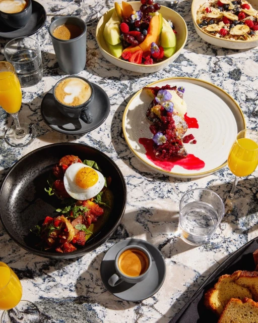 Overhead shot of assorted breakfast foods, including eggs, pastries, fruit, and coffee, arranged on a marble table for a buffet.