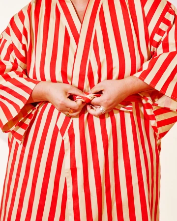 A woman is tying the belt of a red and cream-striped robe with her hands. The close-up image captures only the midsection of the subject.