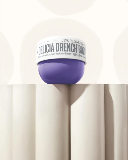 Sol de Janeiro Delicia Drench Body Butter jar in purple and white on a decorative white surface against a cream backdrop.