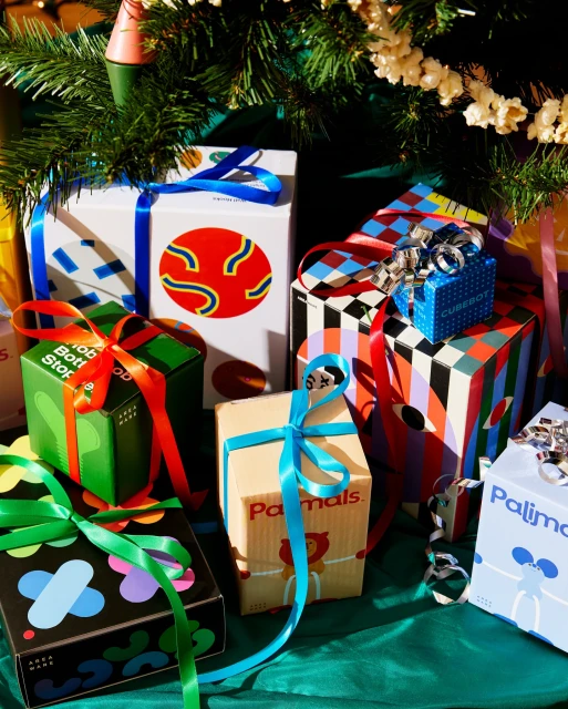 Festive Christmas presents with colorful graphic designs, ribbons, and seasonal decor under a tree, creating a cheerful holiday scene.