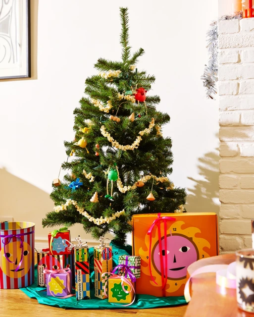 Christmas tree decorated with ornaments and popcorn garland, surrounded by colorful wrapped gifts with cartoon faces. Holiday season indoors.