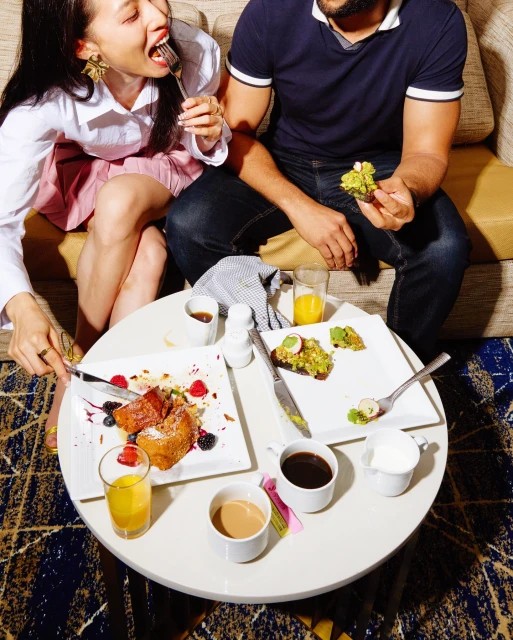 Young couple enjoys brunch with french toast and avocado toast. The table is full of plates, juice, and coffee in bright indoor light.