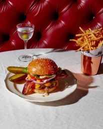 Gourmet cheeseburger with bacon and pickles on a white plate alongside a martini and fries, shot by Emma Fishman.