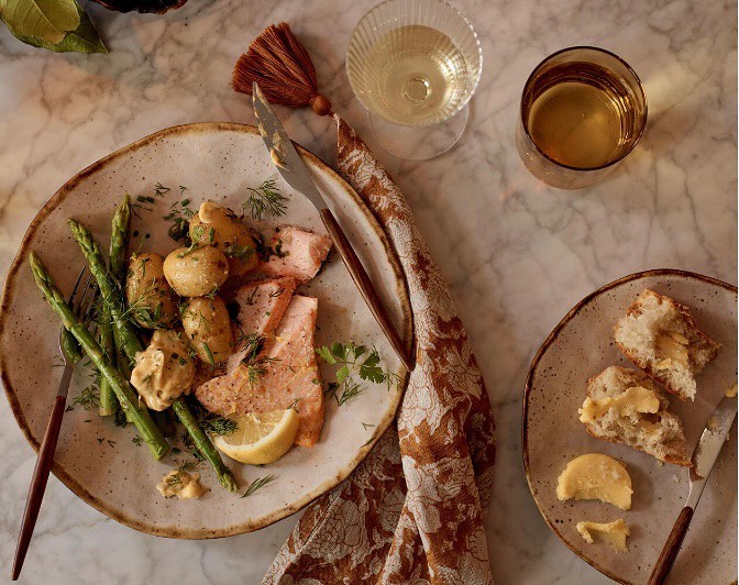 Overhead shot of salmon with potatoes and asparagus plated with bread and wine glasses on a marble surface, showcasing food photography.