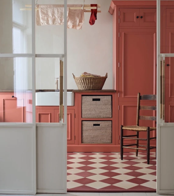 View of terracotta-toned kitchen area with checkered flooring, traditional cabinets, laundry basket, and drying rack with clothes.
