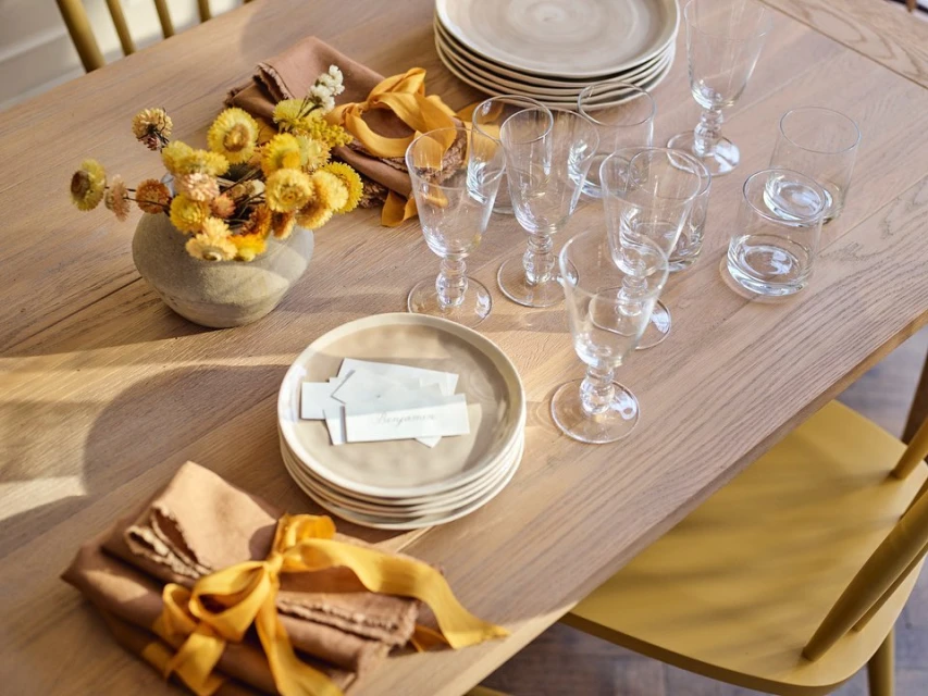 Overhead shot of a dining table setting with plates, glasses, flowers, napkins, and ribbons in a warm, inviting light.