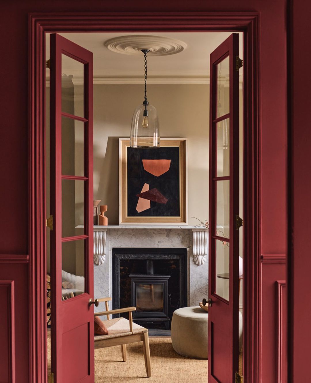 Living room interior featuring red painted walls, fireplace, and modern art, framed by an open doorway. Interior design and home decor.