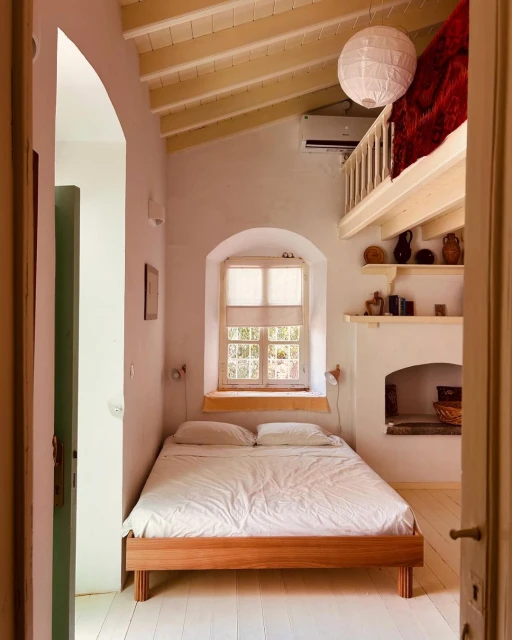 Bedroom interior with a wooden bed frame, white bedding, and a window with natural light, showcasing a simple and inviting space.