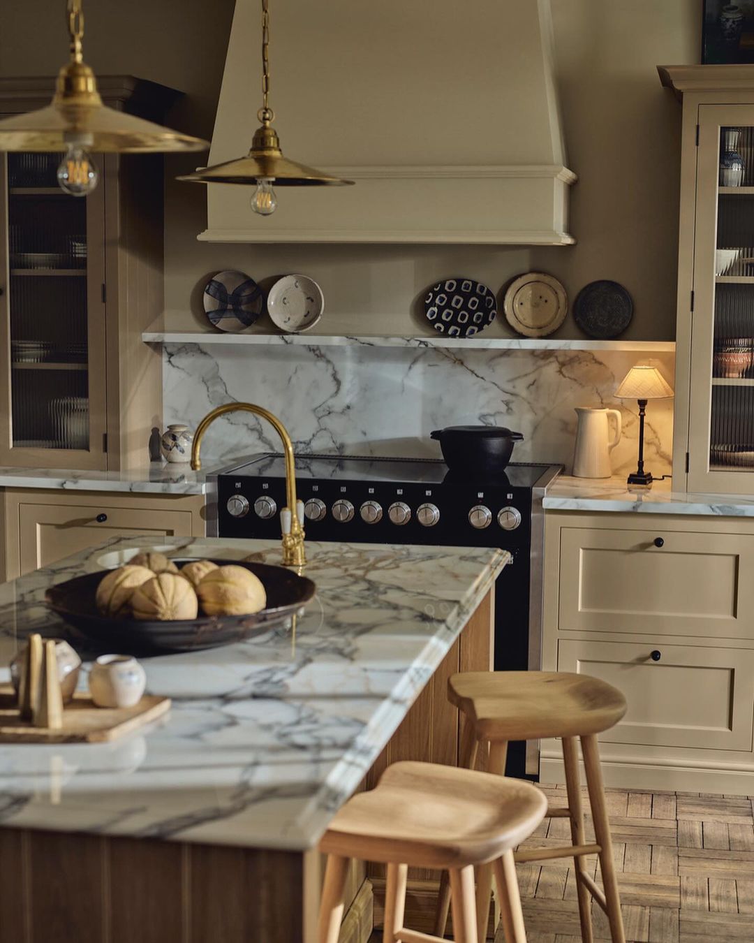 Elegant kitchen interior featuring marble countertops, light wood cabinets, a central island, and brass pendant lights, creating a warm ambiance.