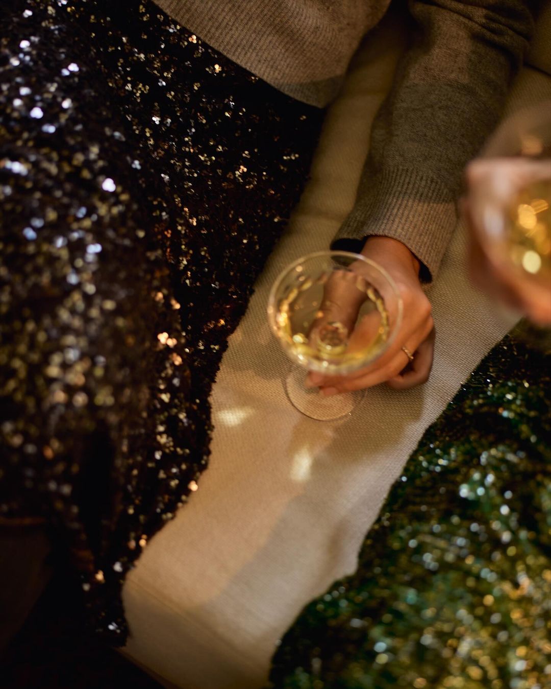 Two women in sparkly outfits hold wine glasses in a dimly lit setting, creating an intimate and festive atmosphere.