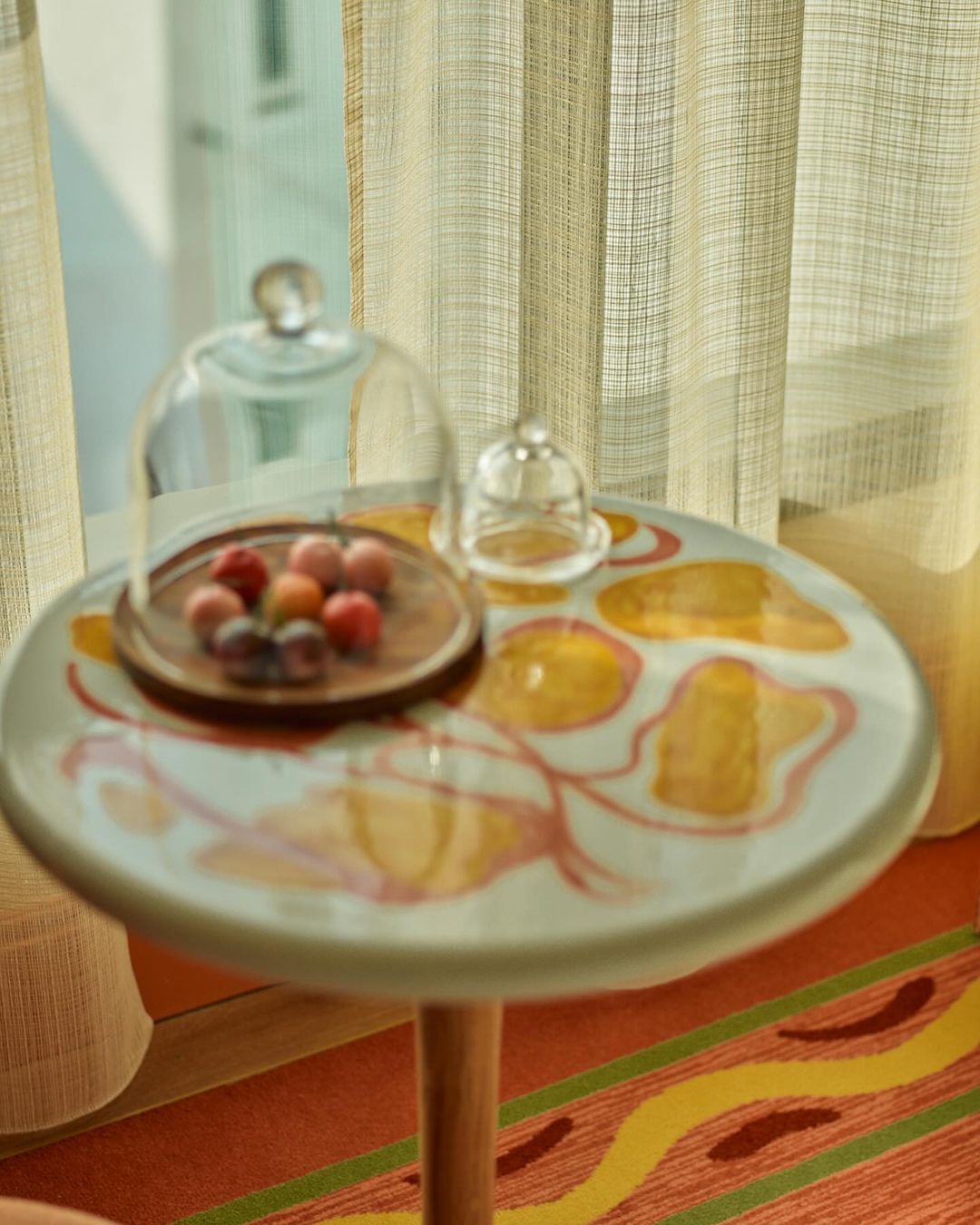 Close-up of small round table with a wood-covered snack tray under glass dome on top of an orange and yellow carpet.