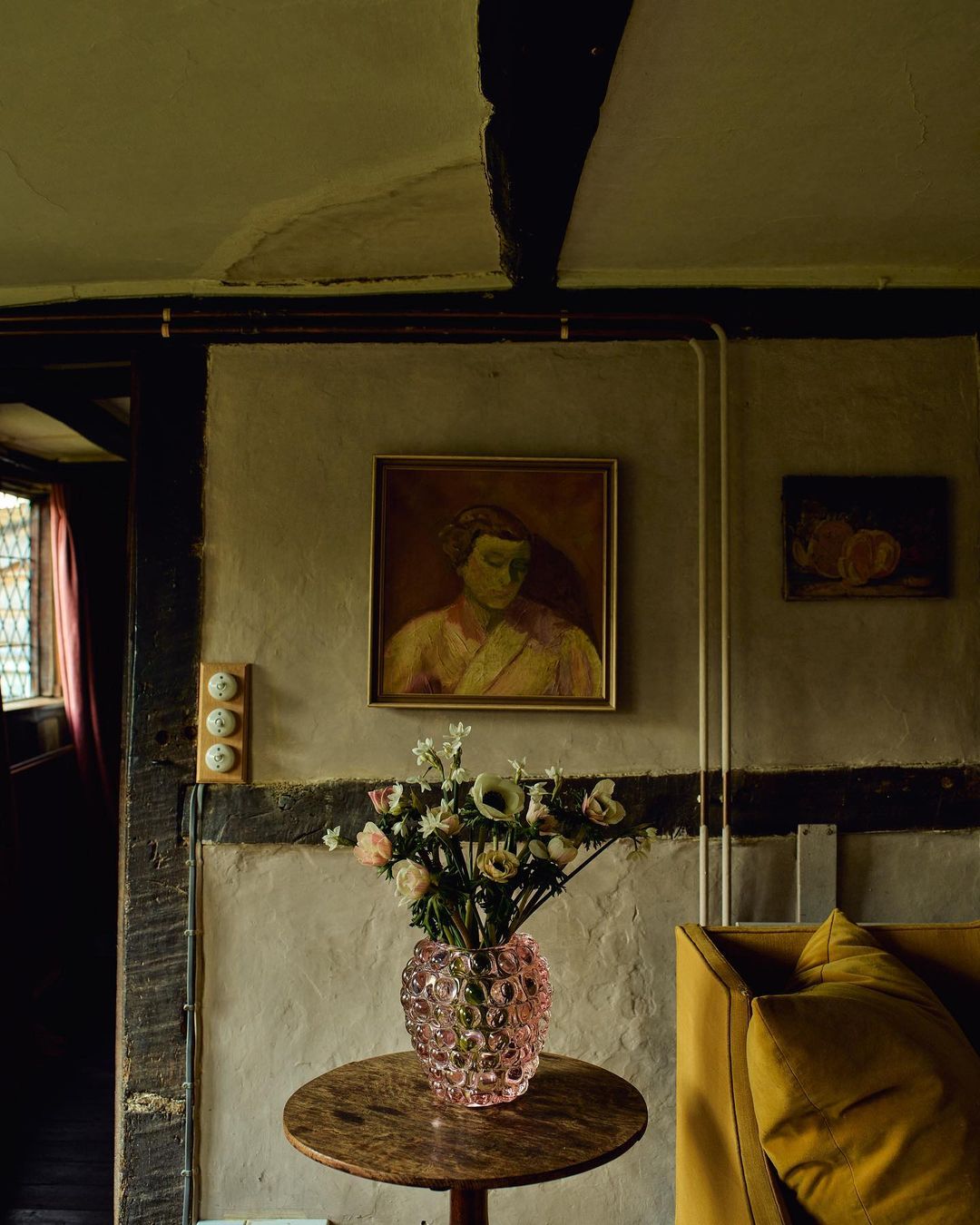 Interior view of a home featuring a table with a flower arrangement, artwork, and part of a yellow sofa, creating a cozy and artistic living space.