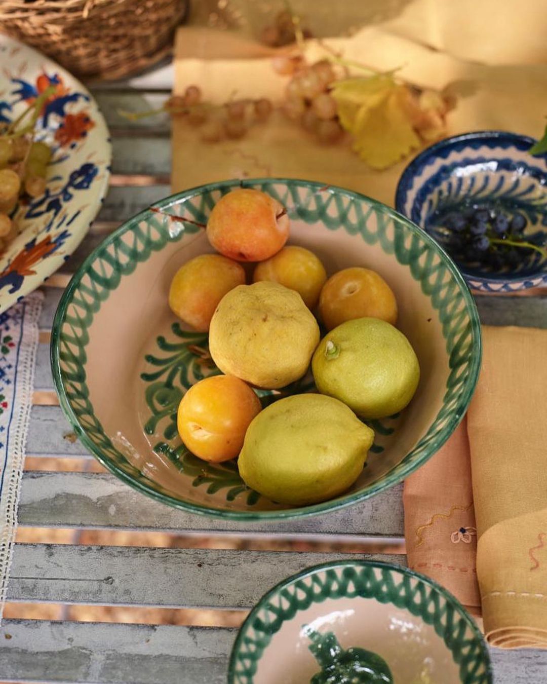 Overhead shot of lemons and apricots in a decorative bowl, with grapes and more dishes in the background on a rustic table.