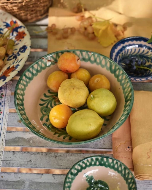Overhead shot of lemons and apricots in a decorative bowl, with grapes and more dishes in the background on a rustic table.