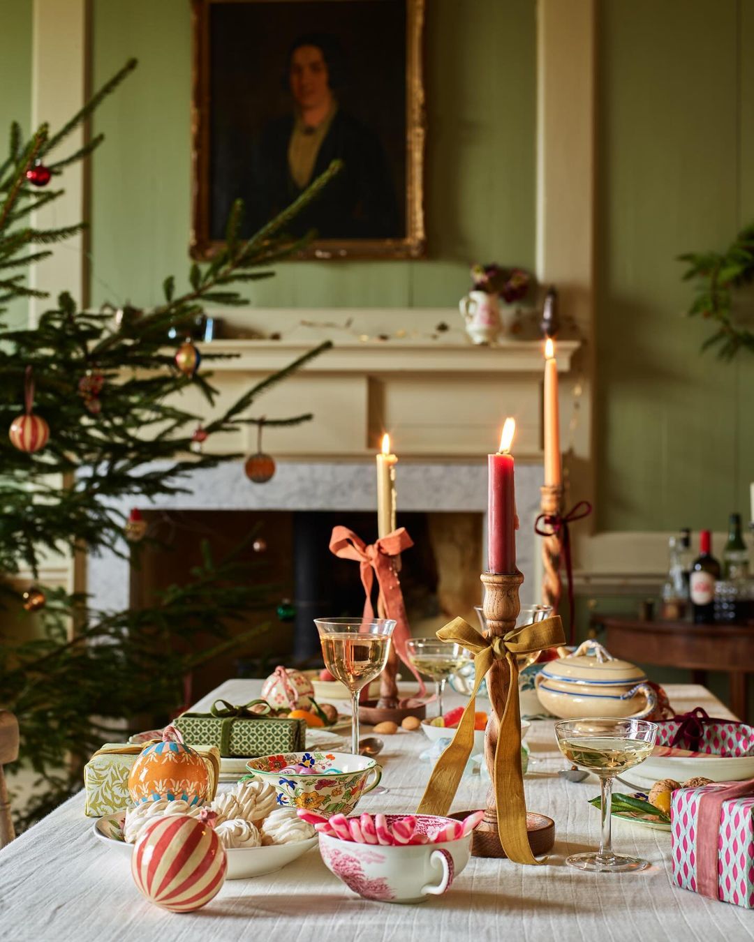Festive table setting with a Christmas tree, candles, glassware, and porcelain dishes creating a warm and inviting holiday atmosphere.
