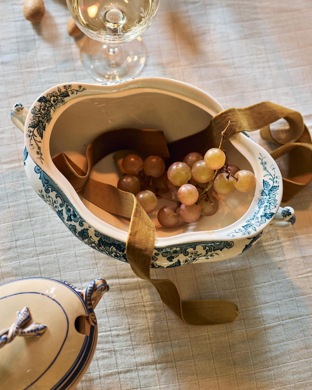 Still life of antique tureen filled with grapes and a champagne flute on a linen tablecloth create a vintage food scene.