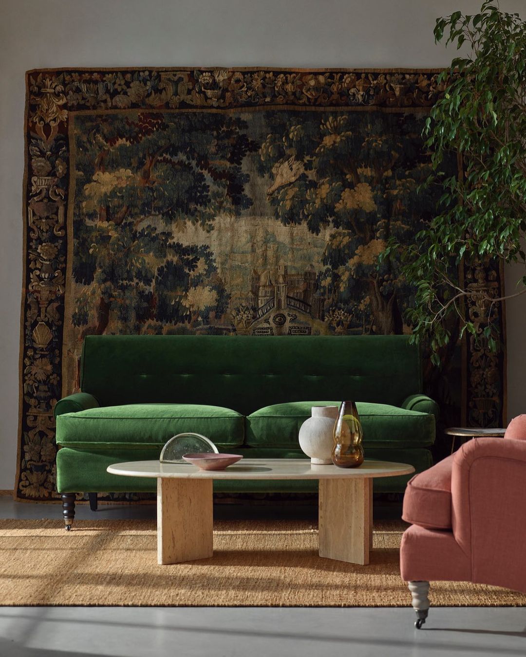 Interior of a living room with a green velvet sofa, a light-colored coffee table, and a tapestry hanging on the wall.