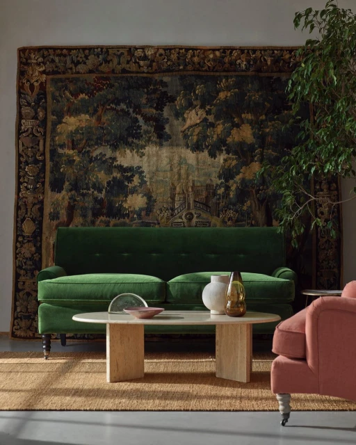Interior of a living room with a green velvet sofa, a light-colored coffee table, and a tapestry hanging on the wall.