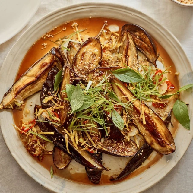 Overhead shot showcases grilled eggplant dish with basil, sesame seeds, and a flavorful sauce, presented on a rustic plate, food photography.