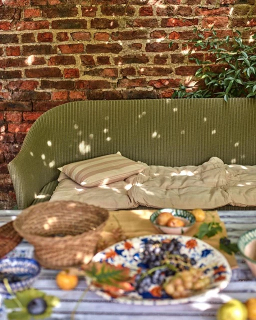 Outdoor lounge area with a green couch, decorative pillows, and a table setting with food and drinks on a sunny day.