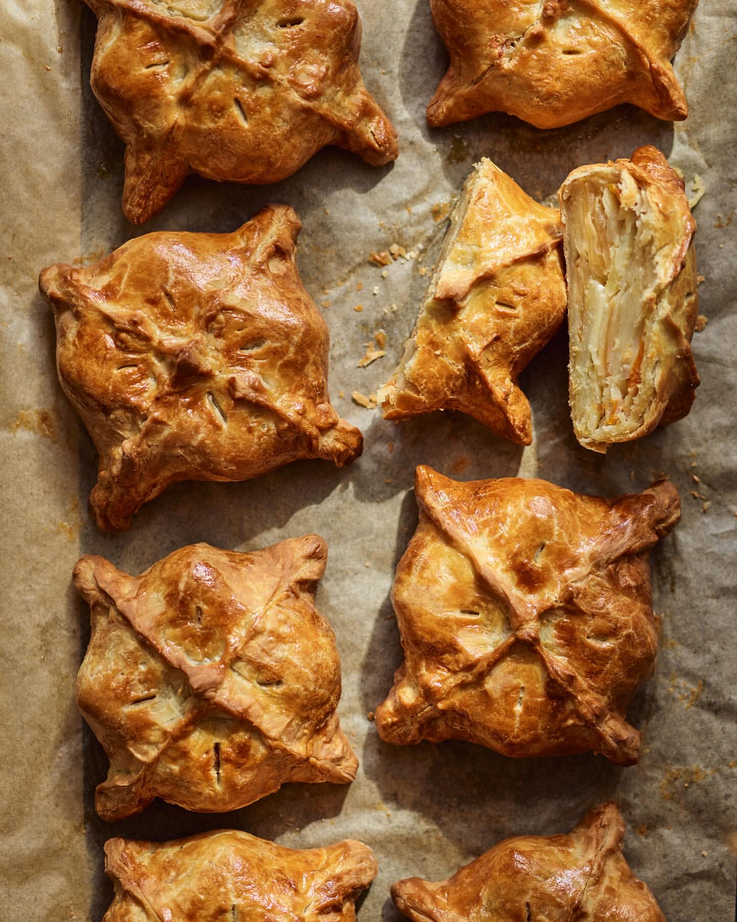 Overhead shot of golden brown pastry squares on parchment paper, some cut to reveal layered filling, creating a warm and inviting food still life.