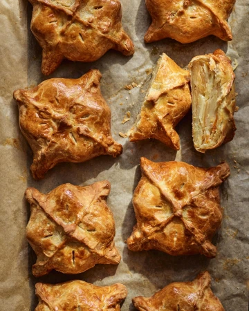 Overhead shot of golden brown pastry squares on parchment paper, some cut to reveal layered filling, creating a warm and inviting food still life.