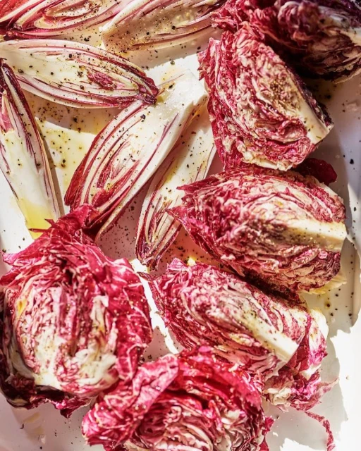 Overhead shot of fresh red radicchio heads and radicchio leaves seasoned and ready to be served on a bright white surface.