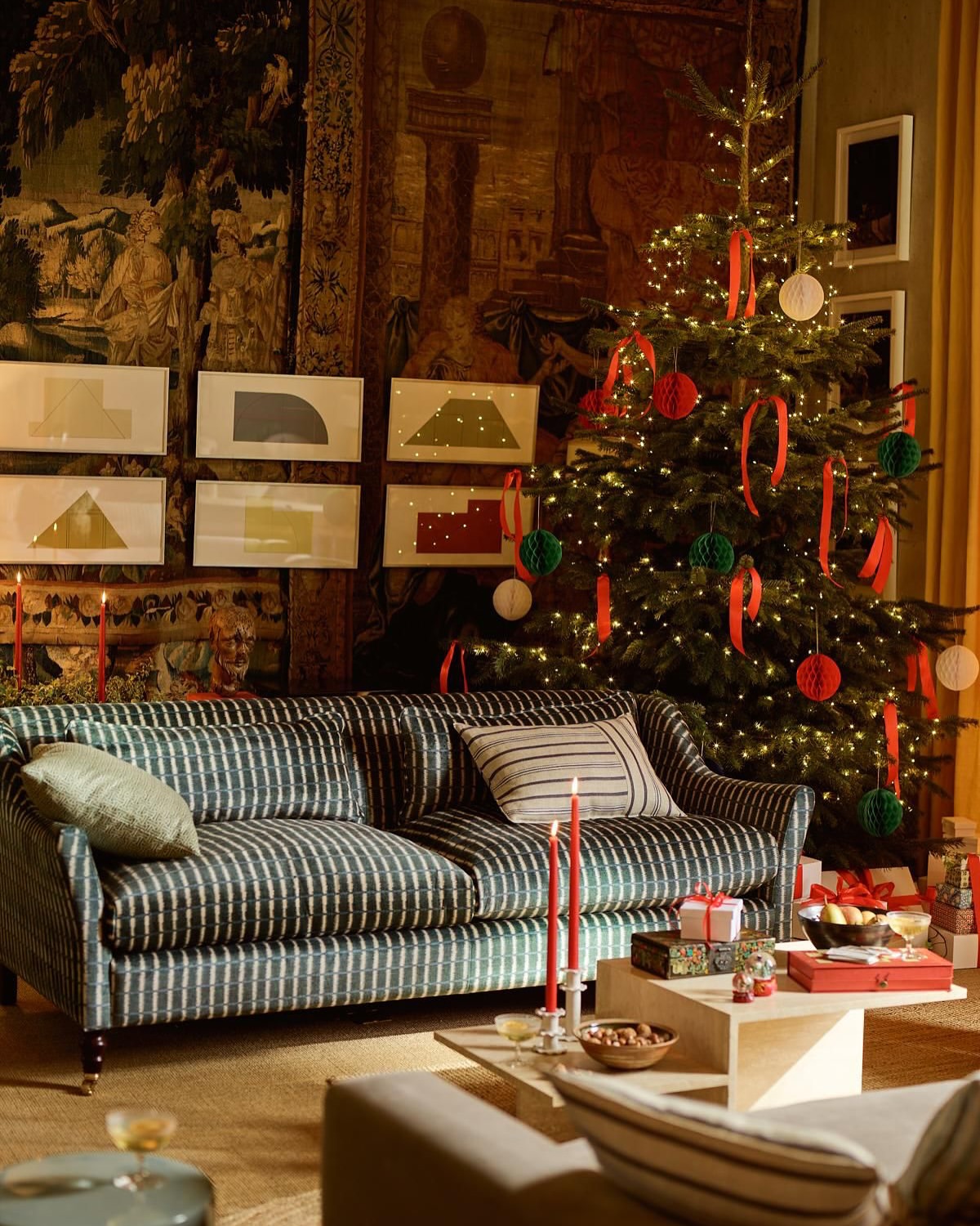 Living room with a Christmas tree decorated with red ribbons and ornaments, sofa, gifts, candles, and framed geometric art.