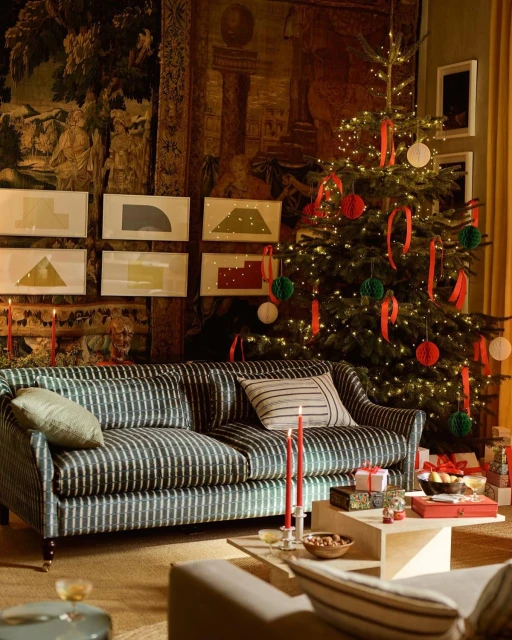Living room with a Christmas tree decorated with red ribbons and ornaments, sofa, gifts, candles, and framed geometric art.