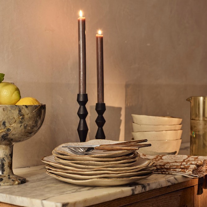 Elevated view of dinnerware set on a marble countertop with candlesticks and citrus fruit adding a warm, inviting ambiance to a dining space.