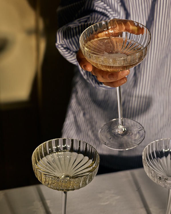 Elegant crystal champagne coupe tower is partially visible, featuring a person in a striped shirt holding the top glass.