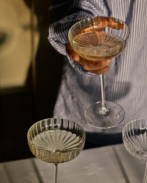 Elegant crystal champagne coupe tower is partially visible, featuring a person in a striped shirt holding the top glass.