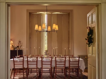 Long wooden dining table set for a formal dinner with candles and wine glasses, lit by a modern multi-arm chandelier in a traditional room.