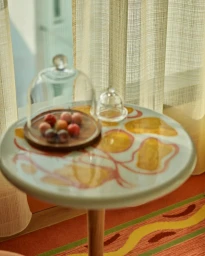Round patterned table with glass cloches and fruits, set against translucent curtains in London by Emma Lee