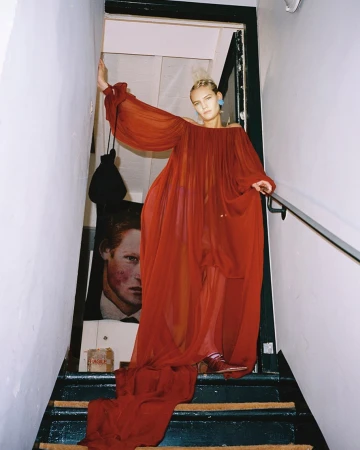 Woman standing on a staircase wearing a flowing red chiffon dress with a long train, photographed by Emma Picq.