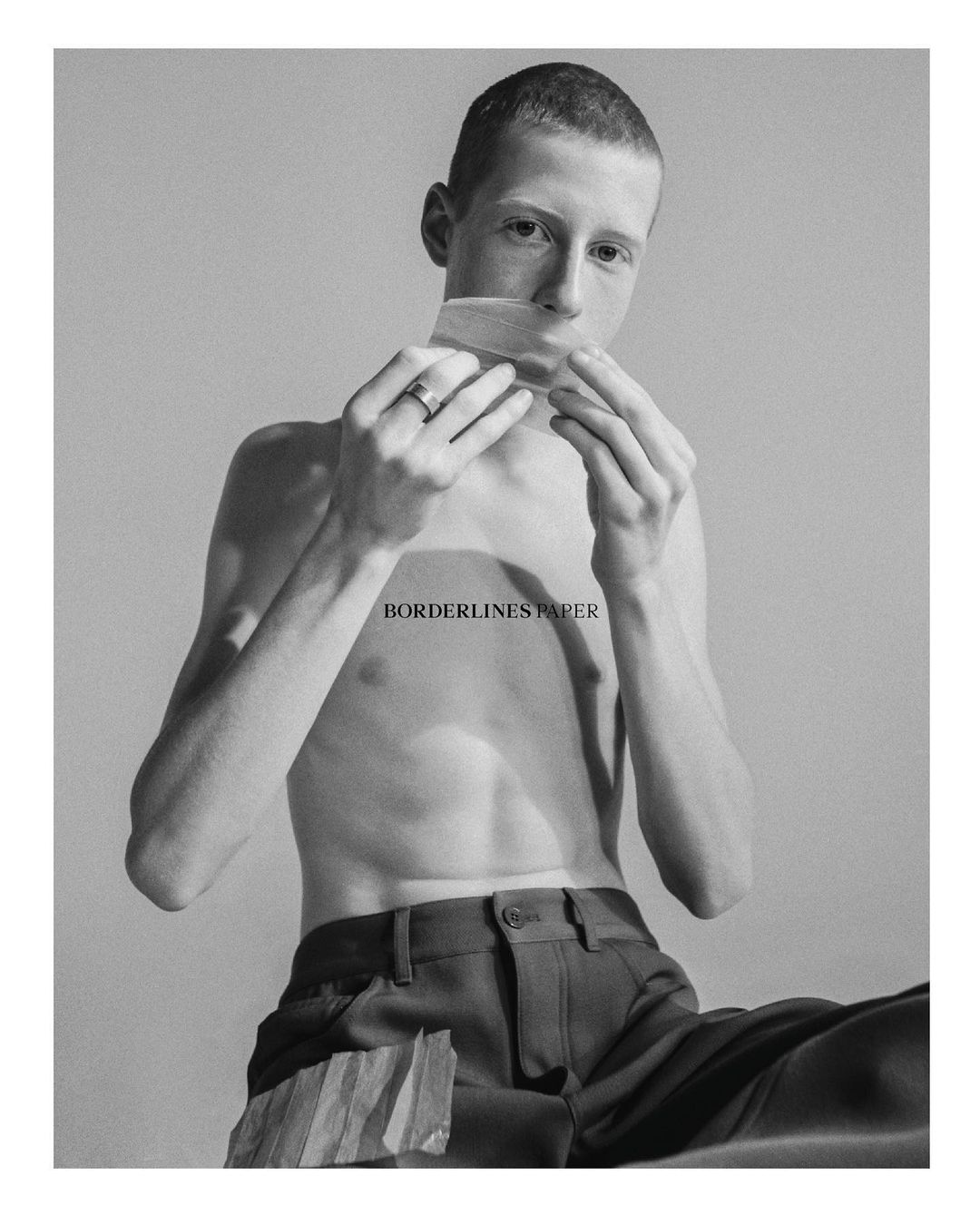 Portrait of a shirtless man with short hair holding a strip of tape over his mouth by Emma Picq
