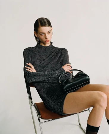 Model with slicked hair seated in a chair wearing a metallic dark grey top and black handbag by Emma Picq