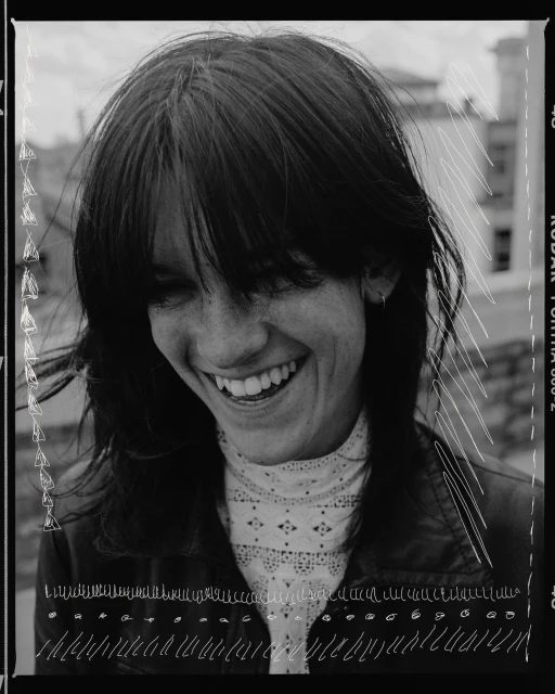 Smiling woman with dark hair and a white lace top, captured in a vintage-style black and white portrait with film border details.
