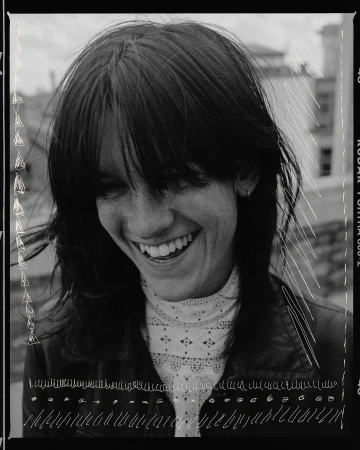 Smiling woman with dark hair and a white lace top, captured in a vintage-style black and white portrait with film border details.