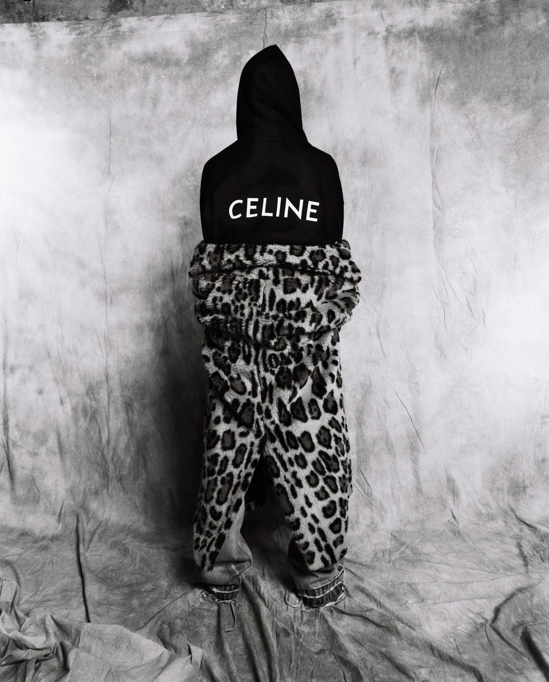 A child in animal-print pants and hooded black Celine sweatshirt, shot in black and white. Features fashion, animal print, and branding.