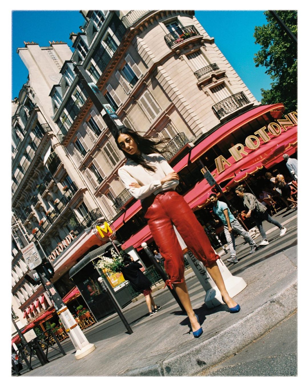 Fashion shot of a woman in red leather pants and a white shirt posing on a street in Paris, France with buildings in the background.