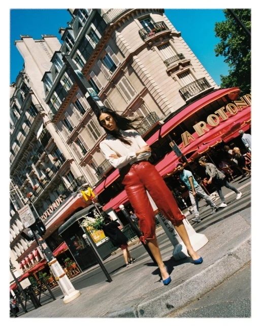Fashion shot of a woman in red leather pants and a white shirt posing on a street in Paris, France with buildings in the background.