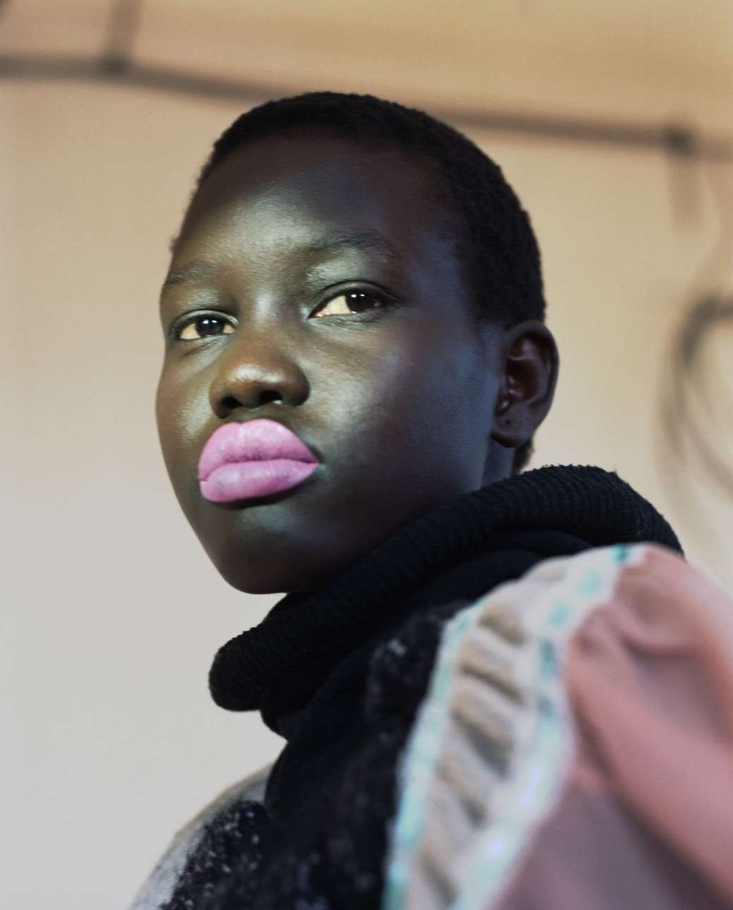 Close-up portrait of a young African female adult with a striking black knit cowl neck, pink lips, and wearing a patterned top.