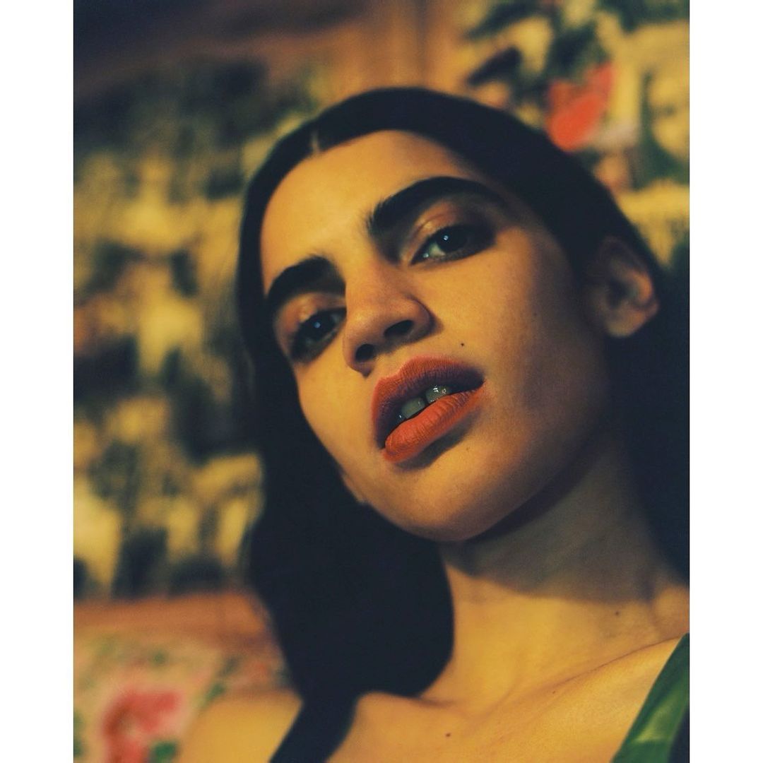 Close-up portrait of a woman with dark hair and coral red lipstick captured from a low angle by photographer Emma Picq in Paris