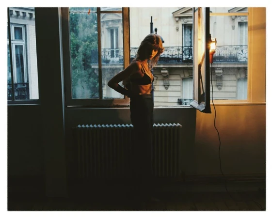 Woman in dark underwear standing by an open window in a Paris interior photographed by Emma Picq