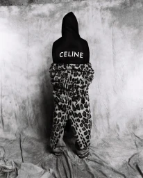 Figure standing backwards wearing a black CELINE hoodie and leopard print trousers against a mottled grey backdrop.
