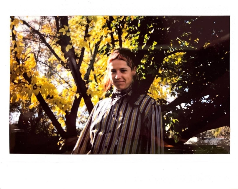 Outdoor portrait of a person in a striped shirt standing in front of trees with yellow leaves on a sunny day. Natural light portrait.