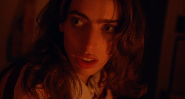 Close-up shot of an adult female with long brown hair and light skin looking up in an orange-lit room, with visible frame edges.