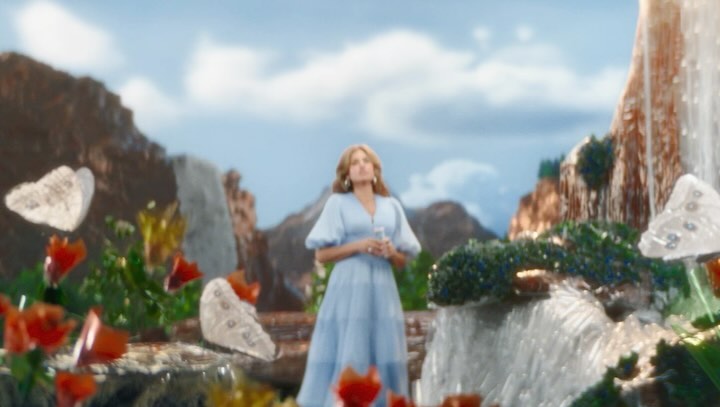 Adult female in a light blue dress stands centered, with waterfalls, butterflies, and mountains visible in an outdoor scenic setting.